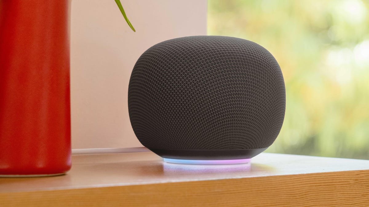 A hazel Google Home Speaker sits on a wood table.