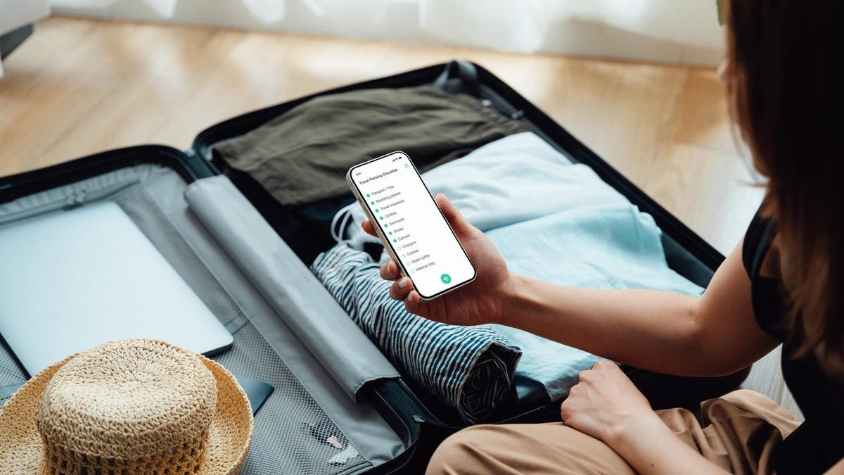 A person packing clothes in luggage looks at an app on their phone.