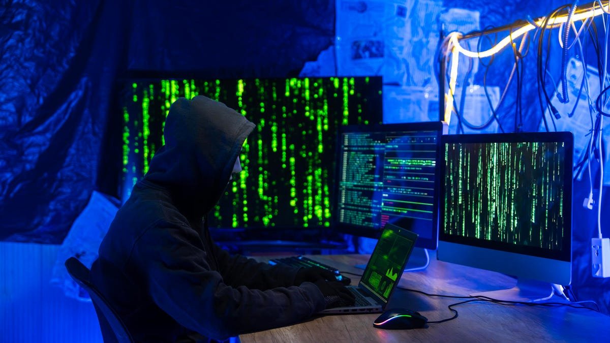 Hacker in Hoodie a Dark Room with Multiple Screens Displaying Code and Data