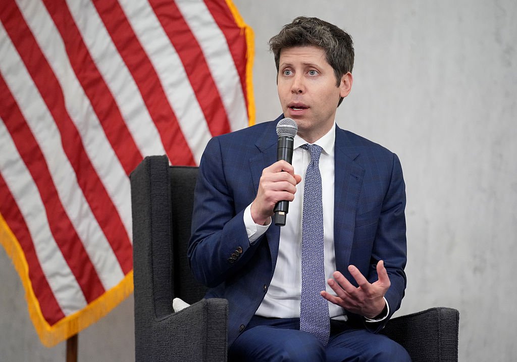 Sam Altman, CEO of OpenAI, sitting in front of American flag