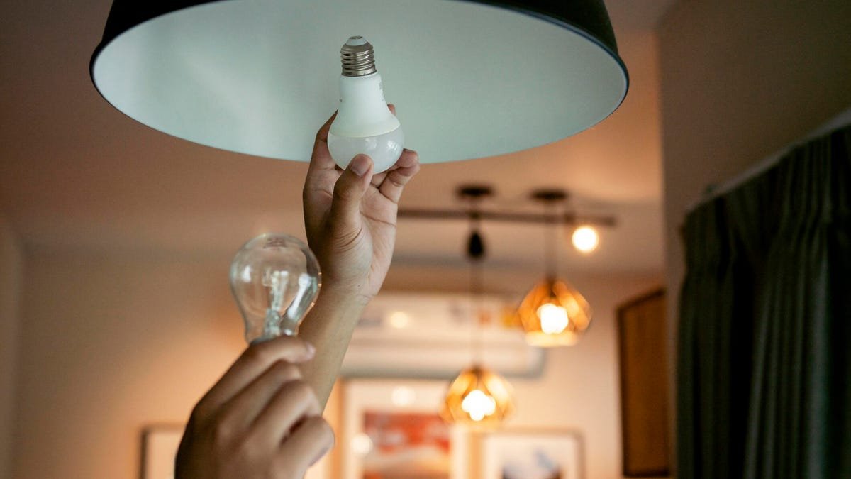 Hands switch an old light bulb out in a home pendant light.