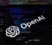 The OpenAI logo is displayed on a smartphone screen placed on a reflective surface onto which lines of computer code.