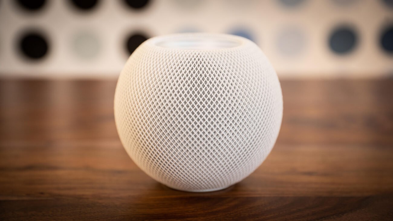 A white HomePod speaker on a wood table.